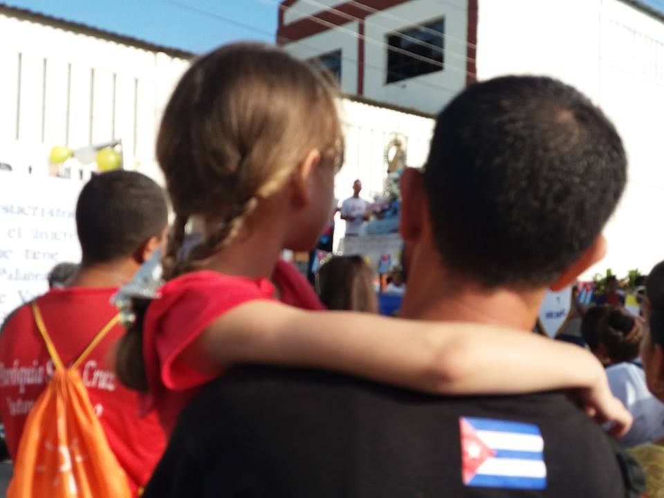 Un padre sostiene a su hija en brazos mientras observa el paso de la cruz